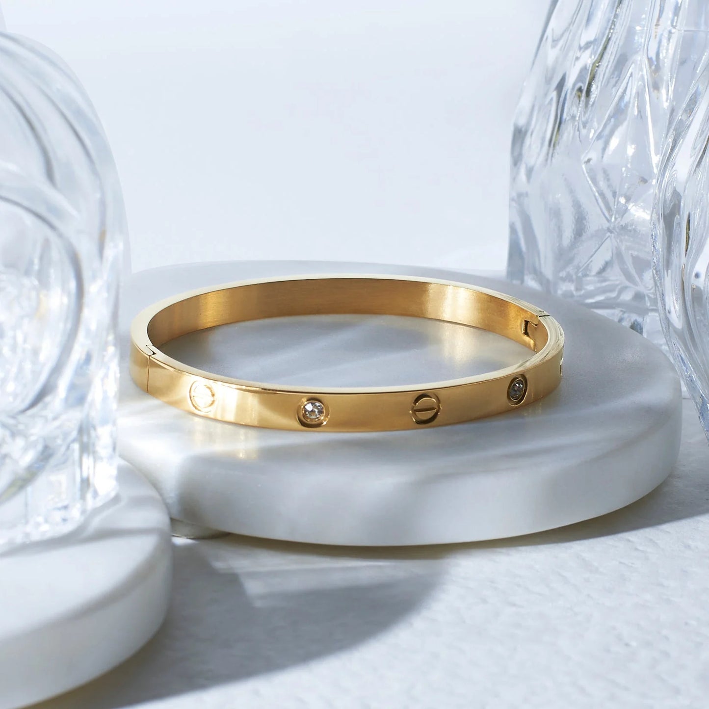 Gold bracelet with embedded stones on a white surface with crystal objects