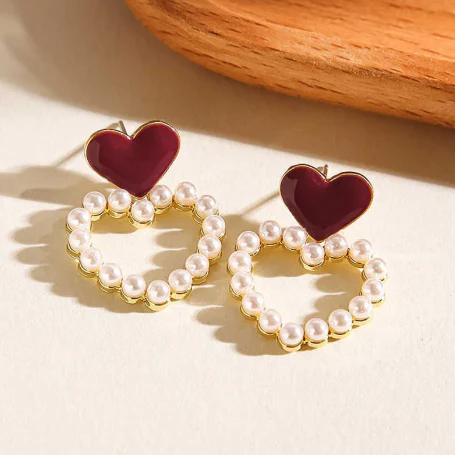 Pair of earrings with red heart-shaped tops and pearl-studded gold loops on a light background.