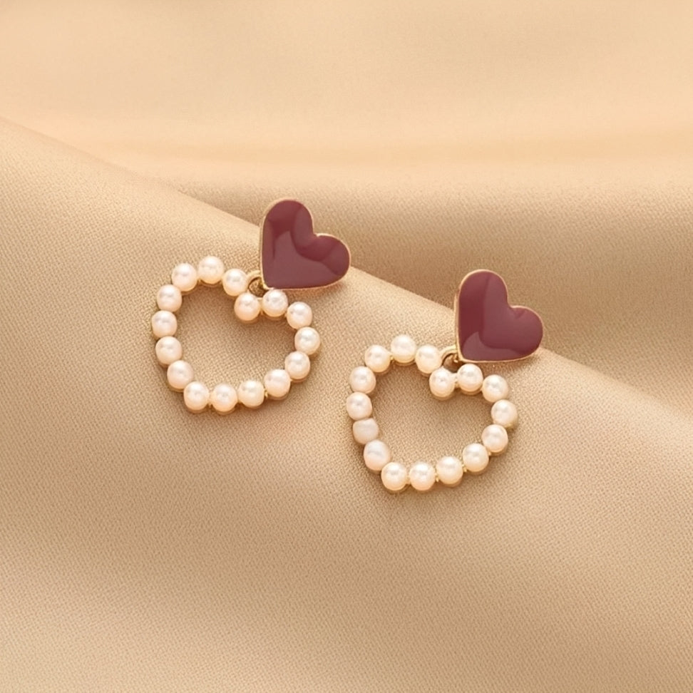 Heart-shaped earrings with pearl-like beads on a beige fabric background