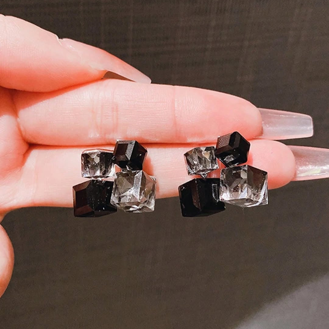 Black and clear crystal earrings held between fingers against a dark background