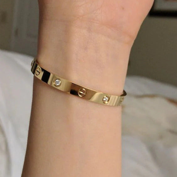 Gold bracelet with diamonds on a wrist against a neutral background