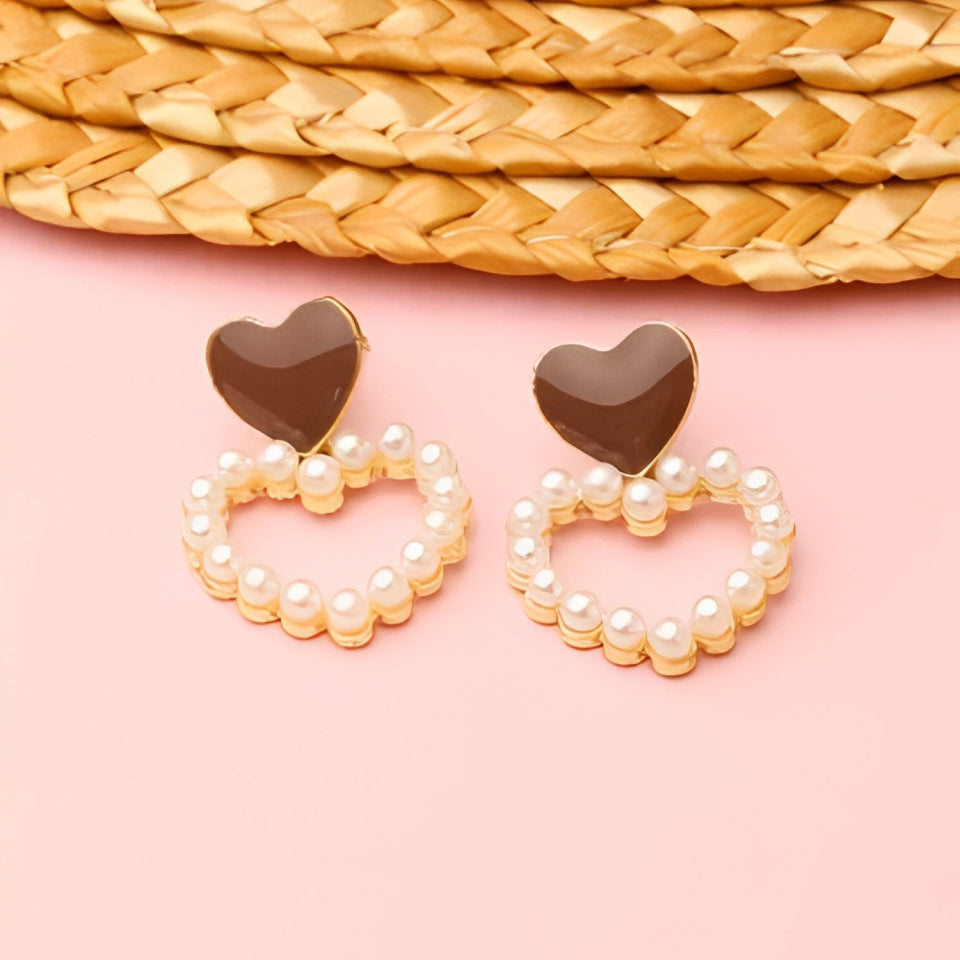 Heart-shaped earrings with pearl detailing on a pink background