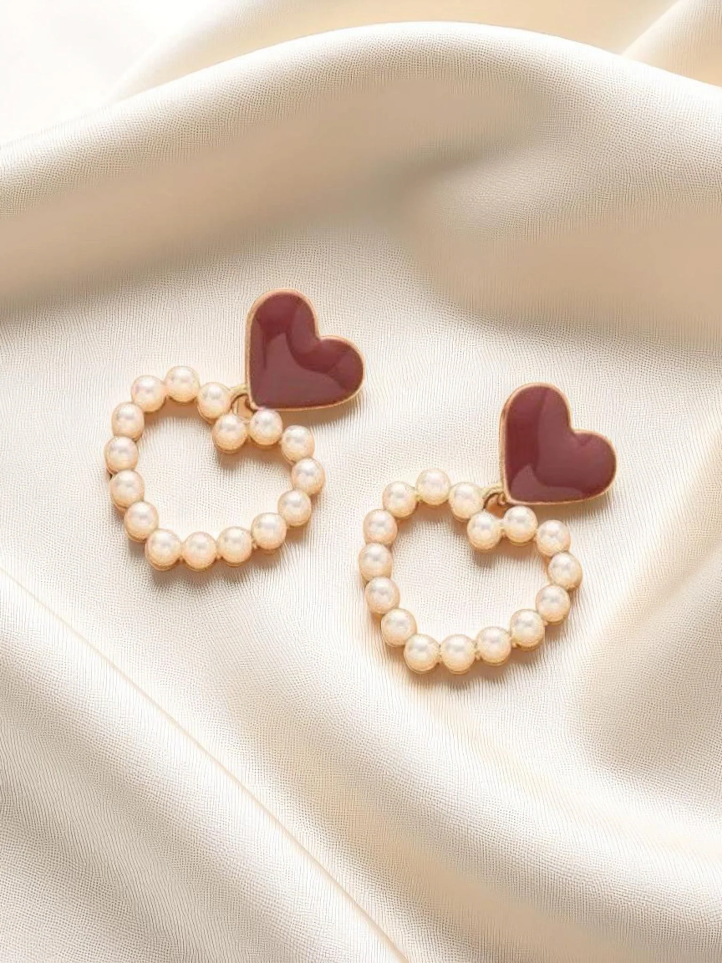 Heart-shaped earrings with pearl details on a soft fabric background