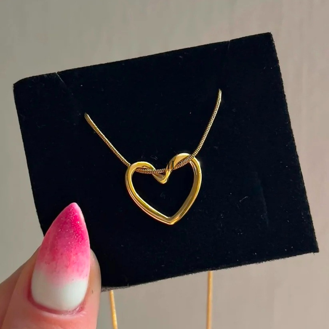 Gold heart-shaped necklace on a black display stand with a hand holding it.