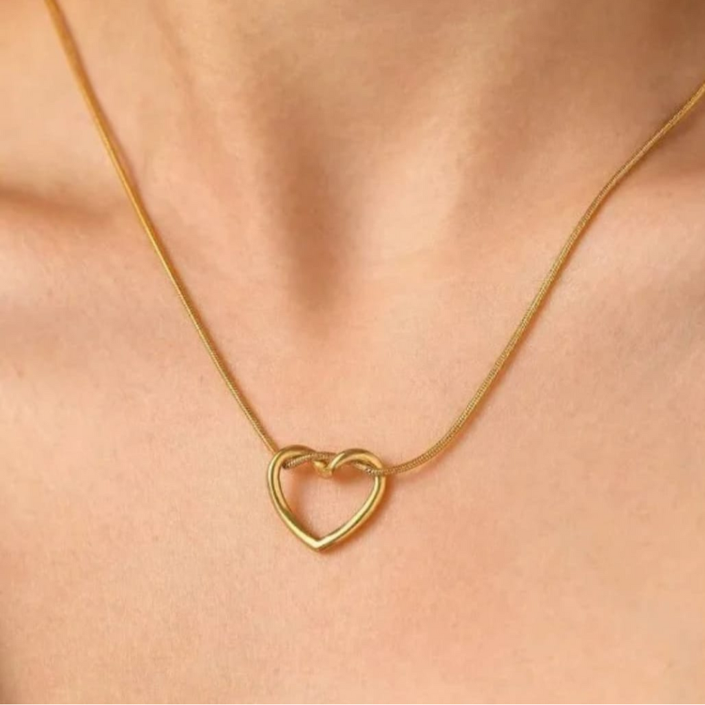 Gold heart-shaped necklace on a person's neck against a neutral background