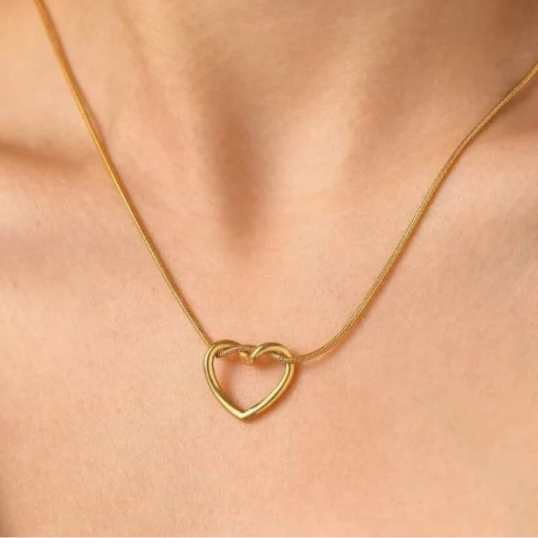 Gold heart-shaped necklace on a person's neck against a neutral background
