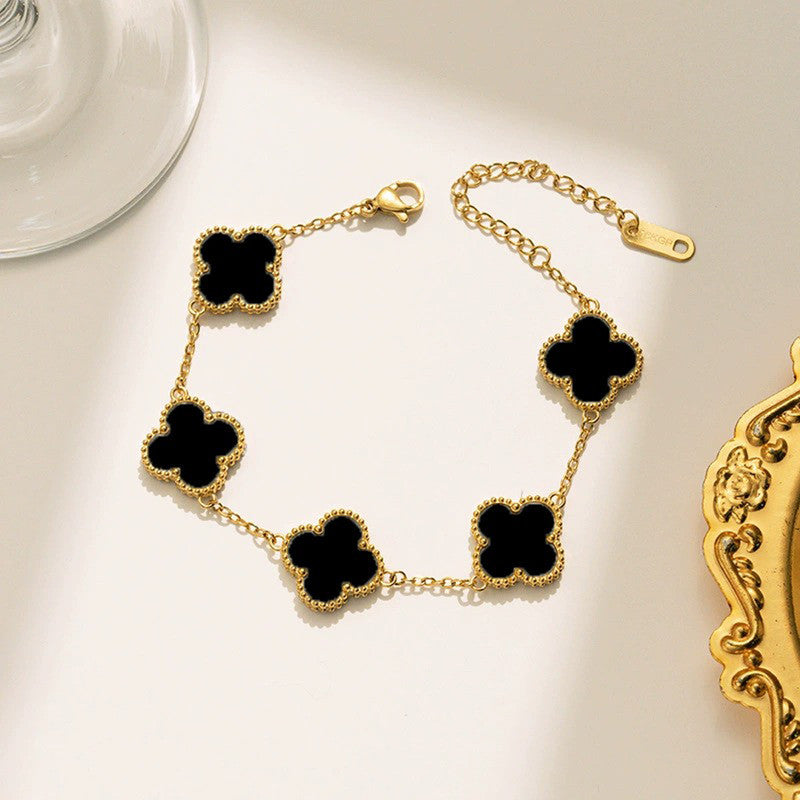 Gold bracelet with black clover-shaped charms on a light surface