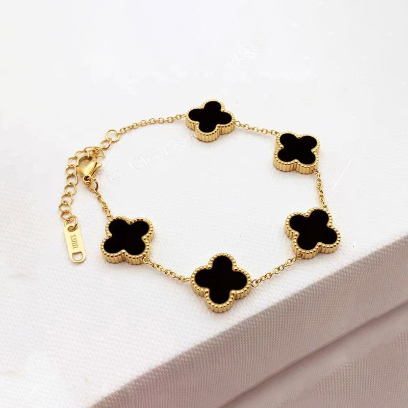 Gold bracelet with black clover-shaped charms on a white background