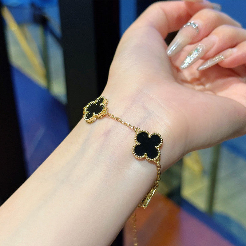 Gold bracelet with black clover-shaped charms on a wrist against a colorful background