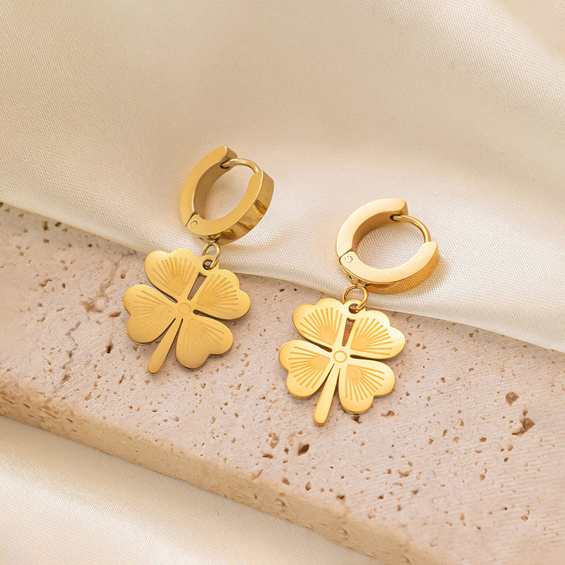 Gold four-leaf clover earrings on a textured beige surface