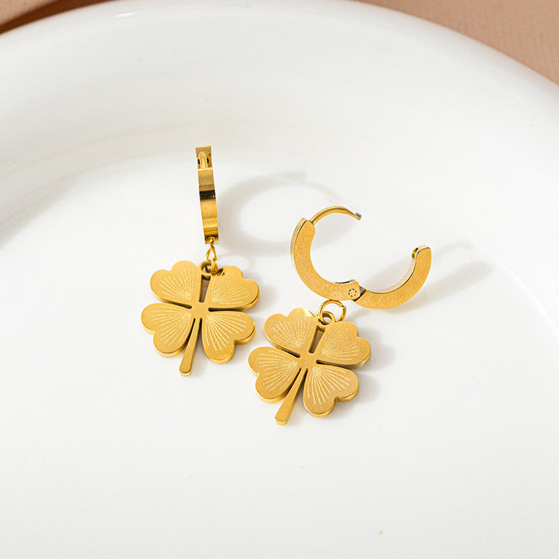Gold four-leaf clover earrings on a white plate