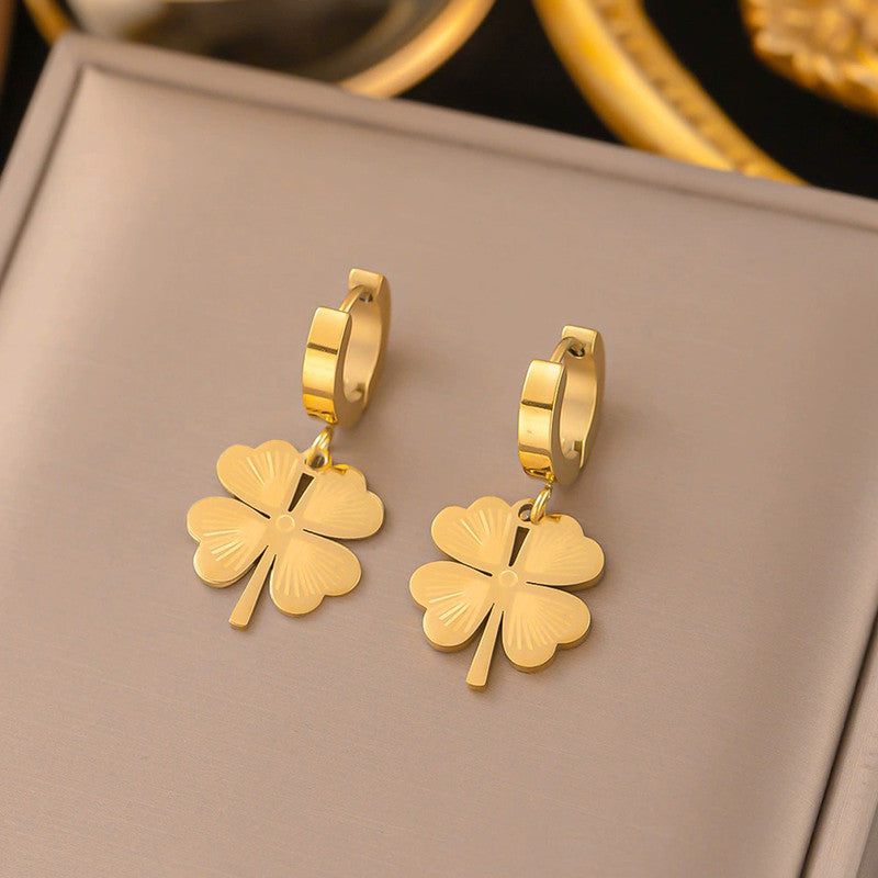 Gold four-leaf clover earrings on a beige surface