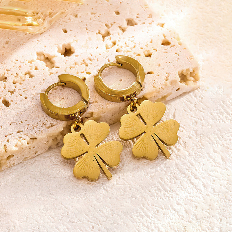 Gold hoop earrings with four-leaf clover charms on a textured beige surface