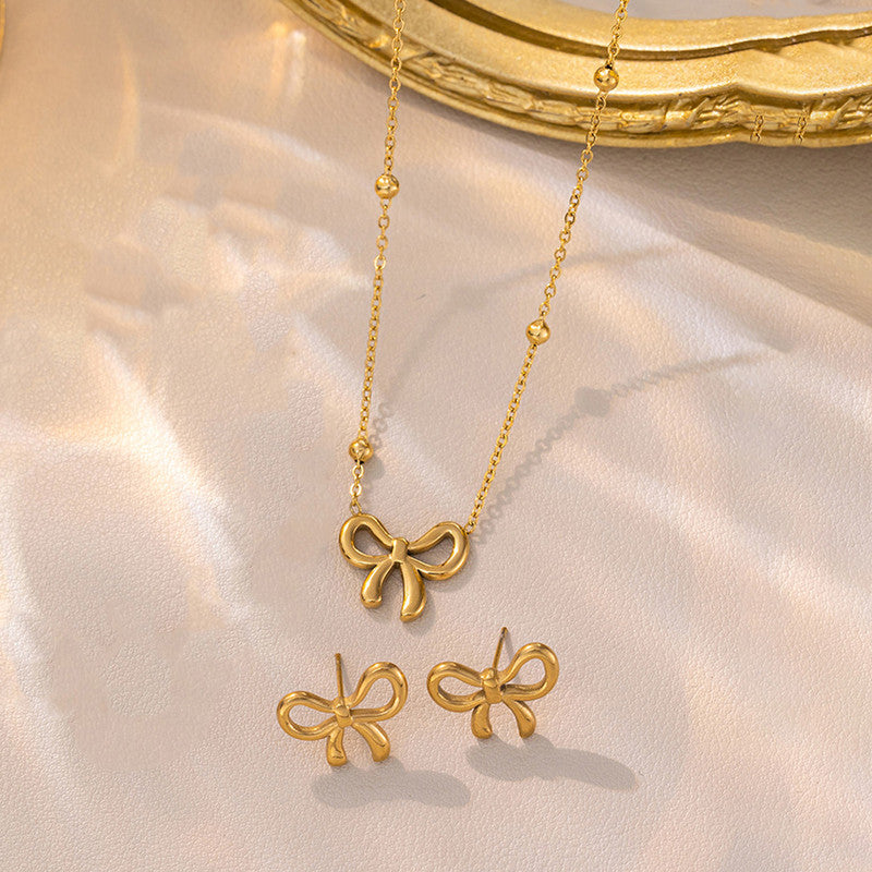 Gold bow-shaped necklace and earrings on a soft pink background