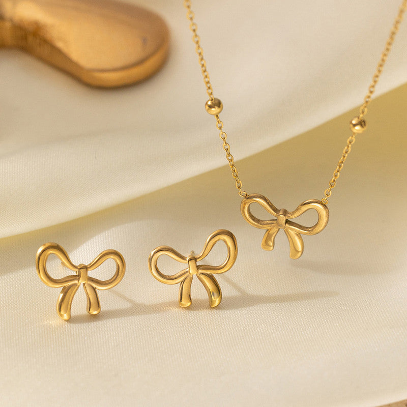 Gold bow-shaped jewelry set on a beige background