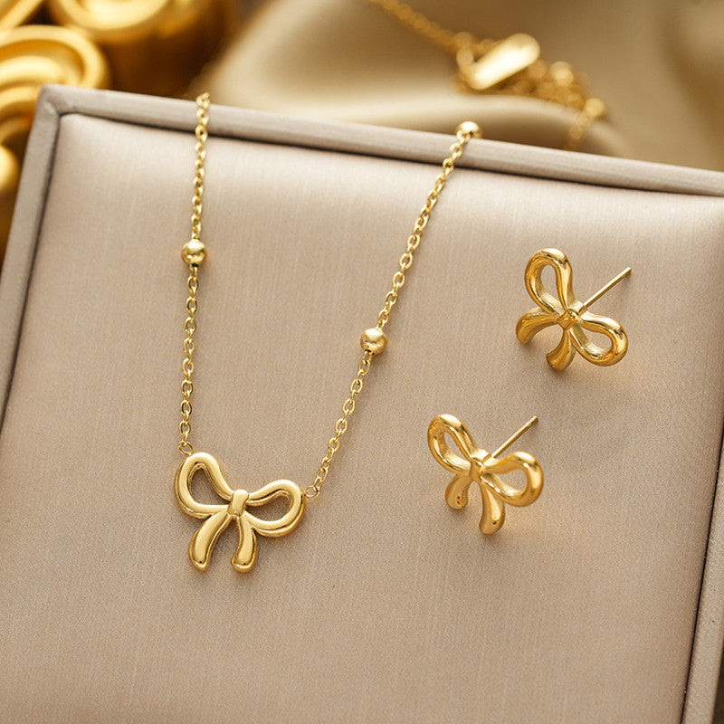 Gold bow-shaped necklace and earrings on a beige jewelry box