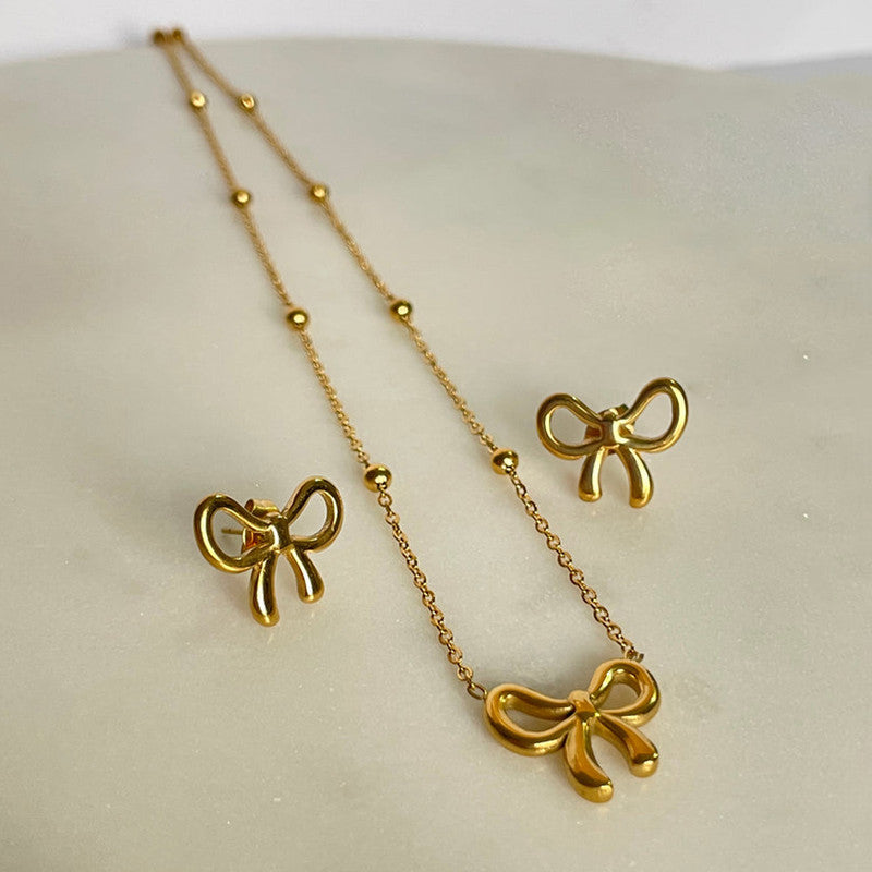 Gold bow-shaped necklace and earrings on a light background