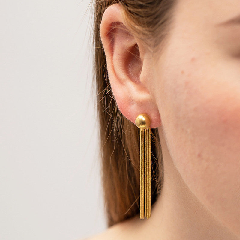 Gold tassel earring worn by a person on a plain background