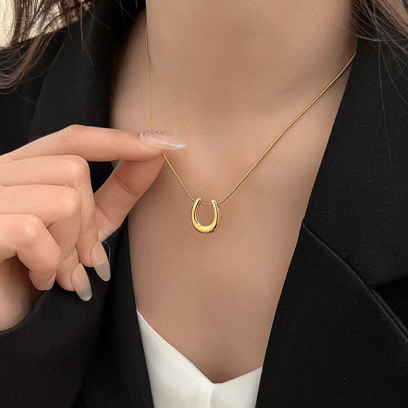 Gold horseshoe necklace being worn and pointed to by a hand