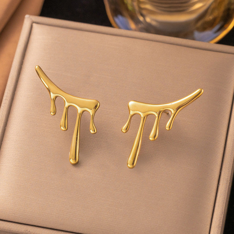 Gold earrings shaped like dripping gold on a beige box