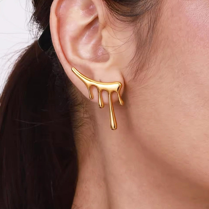 Gold earring with a unique design worn on an ear against a neutral background
