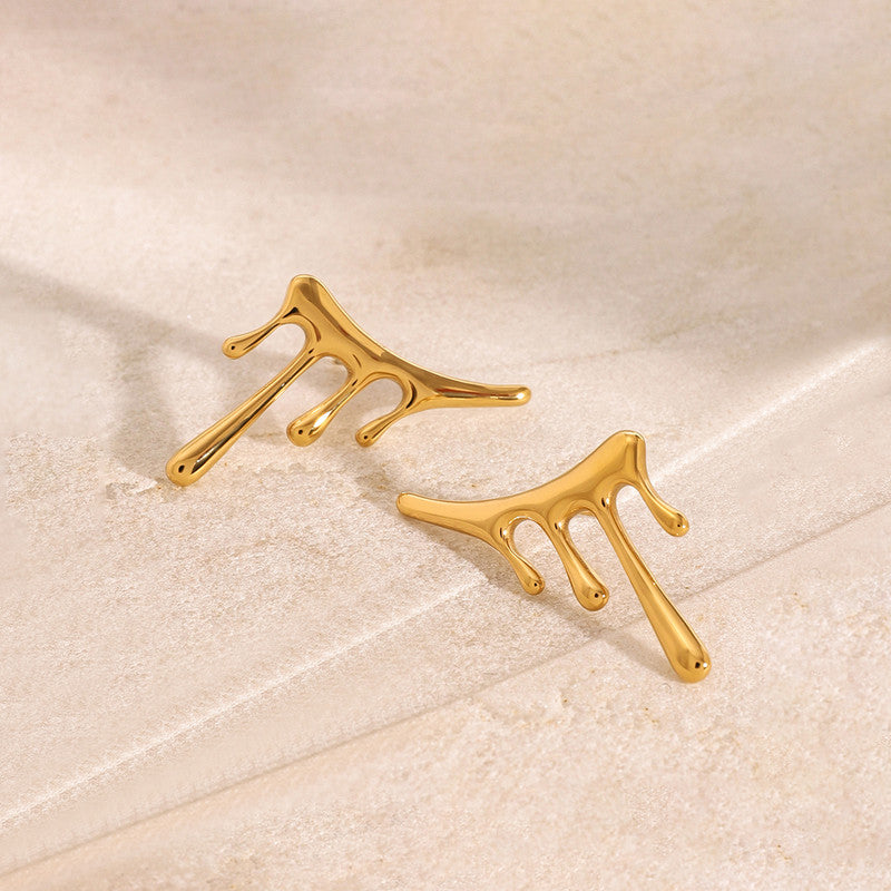 Gold branch-like earrings on a beige surface