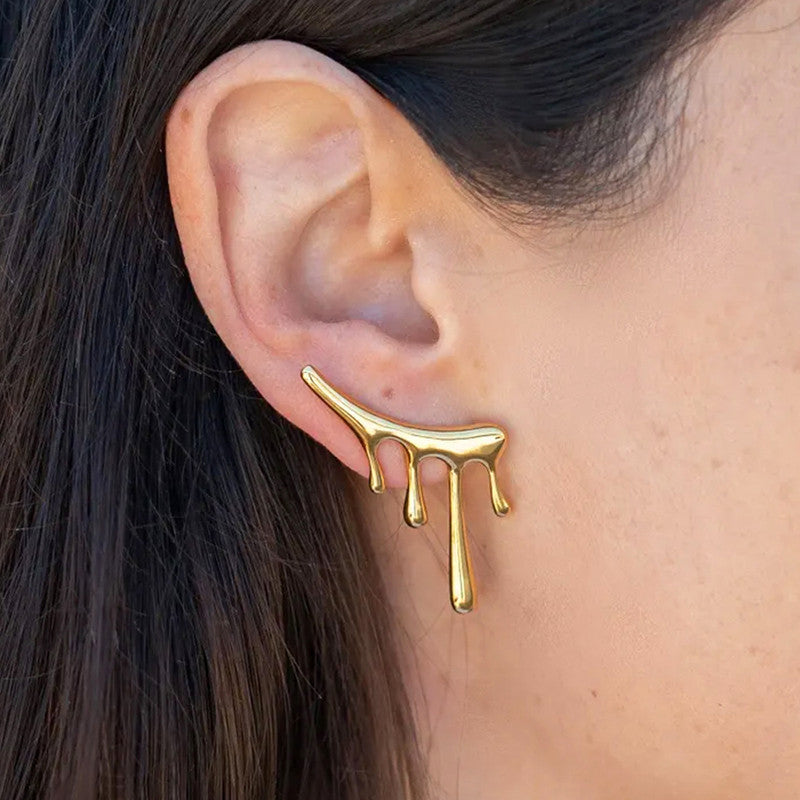 Gold earring with a dripping design worn on an ear