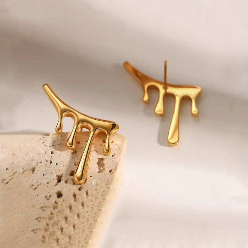 Gold branch-shaped earrings on a textured beige surface