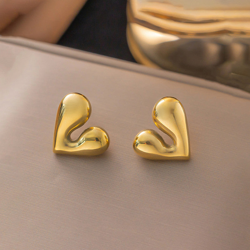 Gold heart-shaped earrings on a beige surface