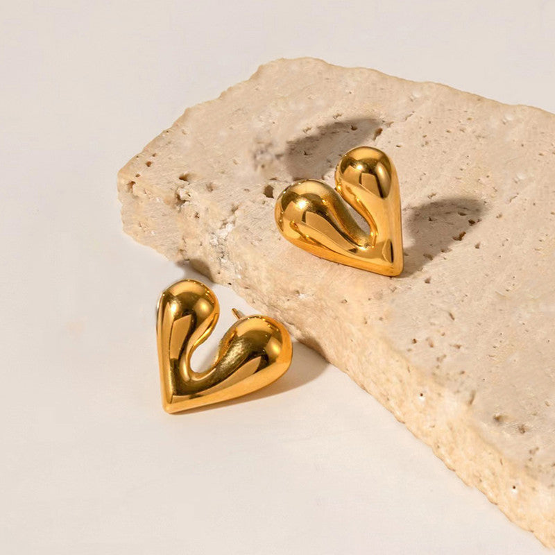 Gold heart-shaped earrings on a beige stone surface
