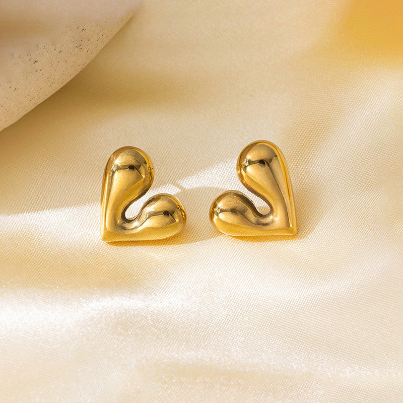 Gold heart-shaped earrings on a beige fabric background