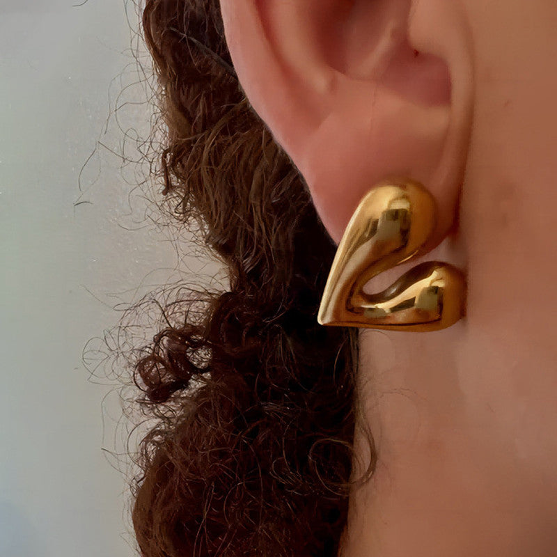 Gold earring worn on an ear with a neutral background