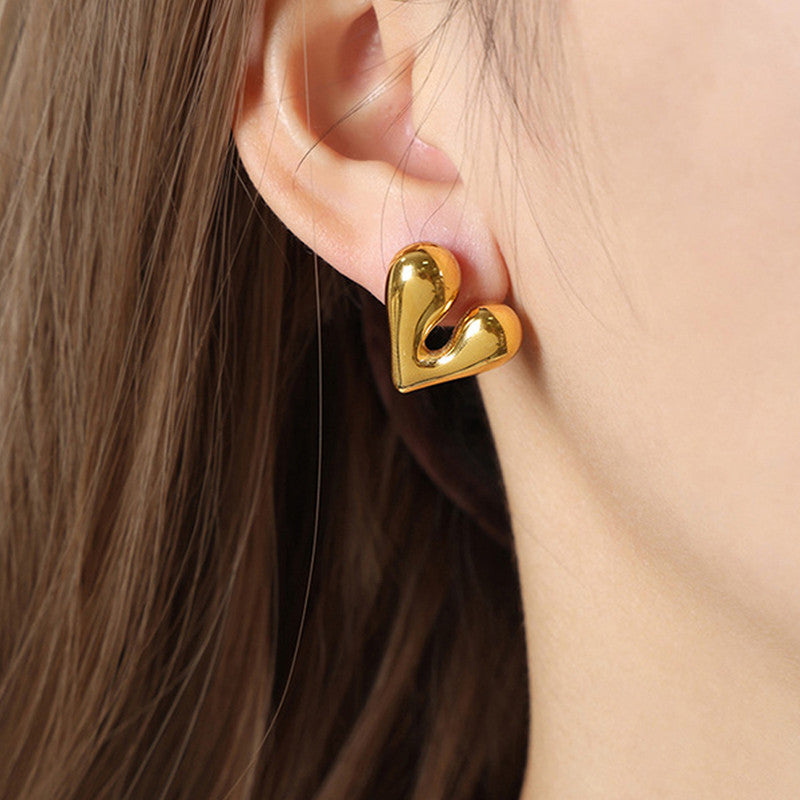 Gold heart-shaped earrings worn by a person with brown hair.
