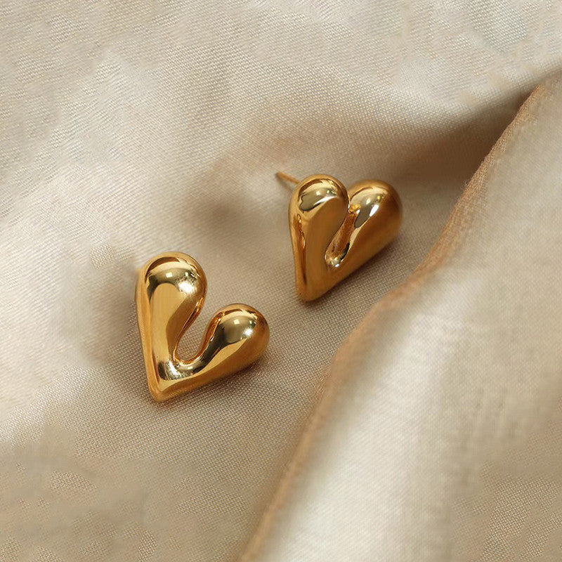 Gold heart-shaped earrings on a beige fabric background