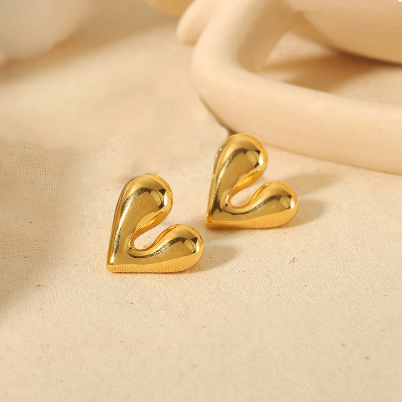 Gold heart-shaped earrings on a beige fabric background