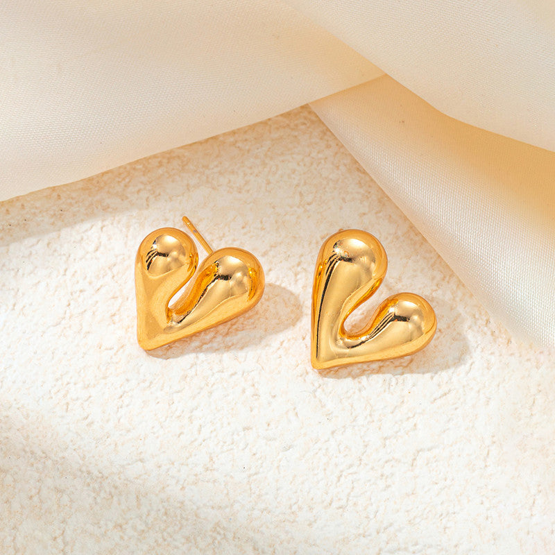 Gold heart-shaped earrings on a textured beige surface