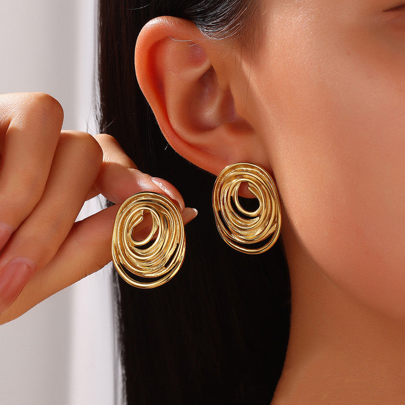 Gold spiral earrings being worn and held up to an ear against a neutral background