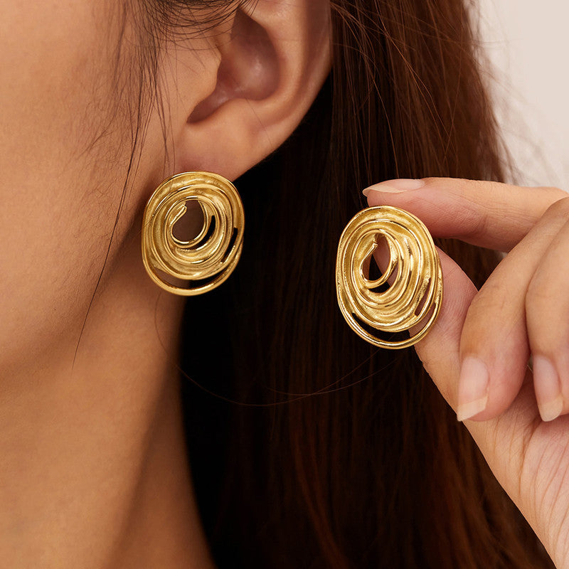 Close-up of a person wearing gold spiral earrings with a hand adjusting one.