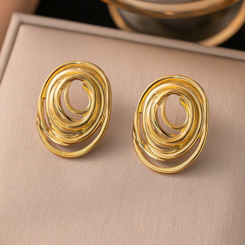 Gold spiral earrings on a beige surface