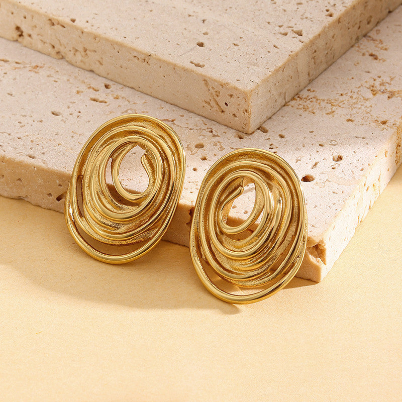 Gold spiral earrings on a beige stone surface