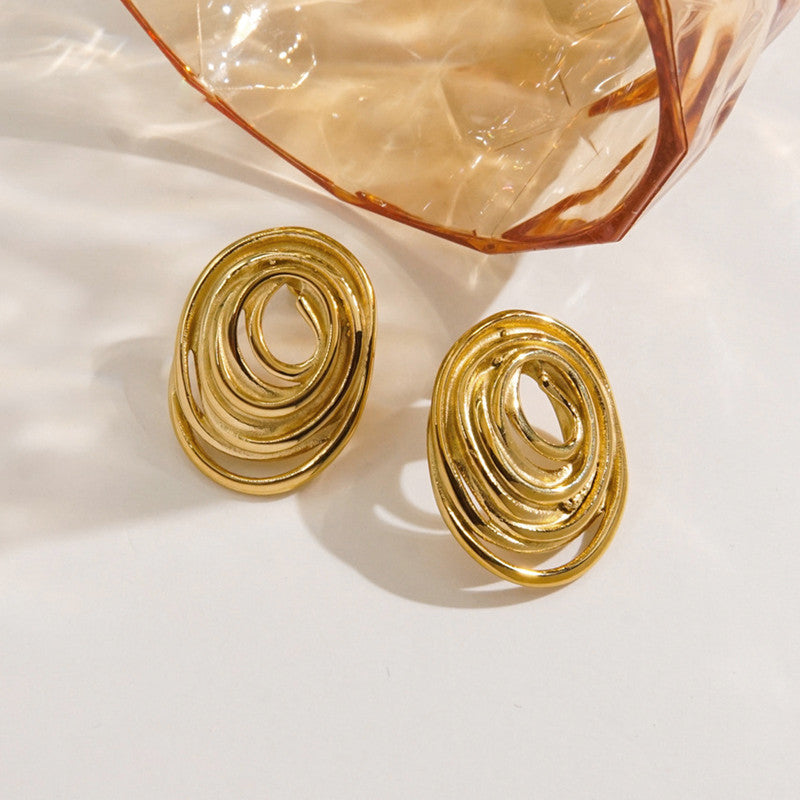 Gold spiral earrings on a light background with a glass container.