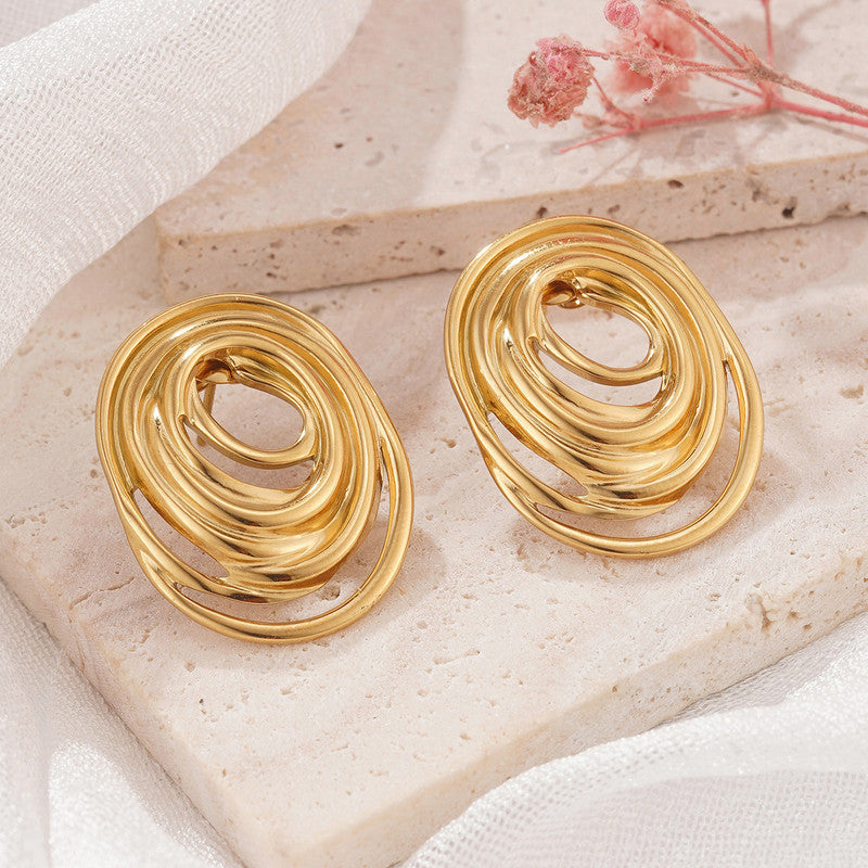 Gold spiral earrings on a stone surface with a soft background
