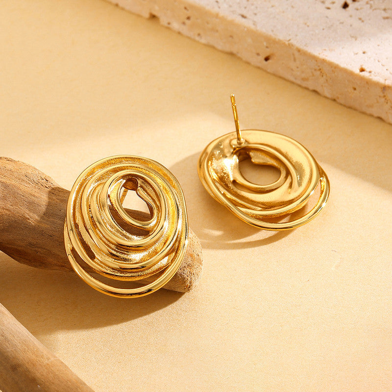 Gold spiral earrings on a beige surface with natural light