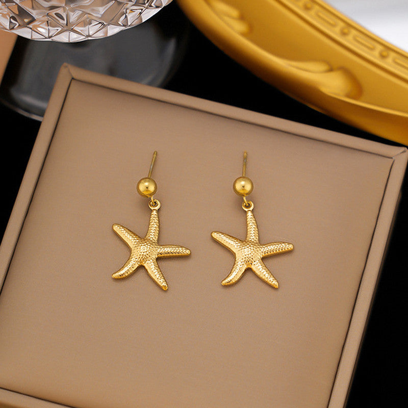 Gold starfish earrings on a brown jewelry box with a gold case in the background.