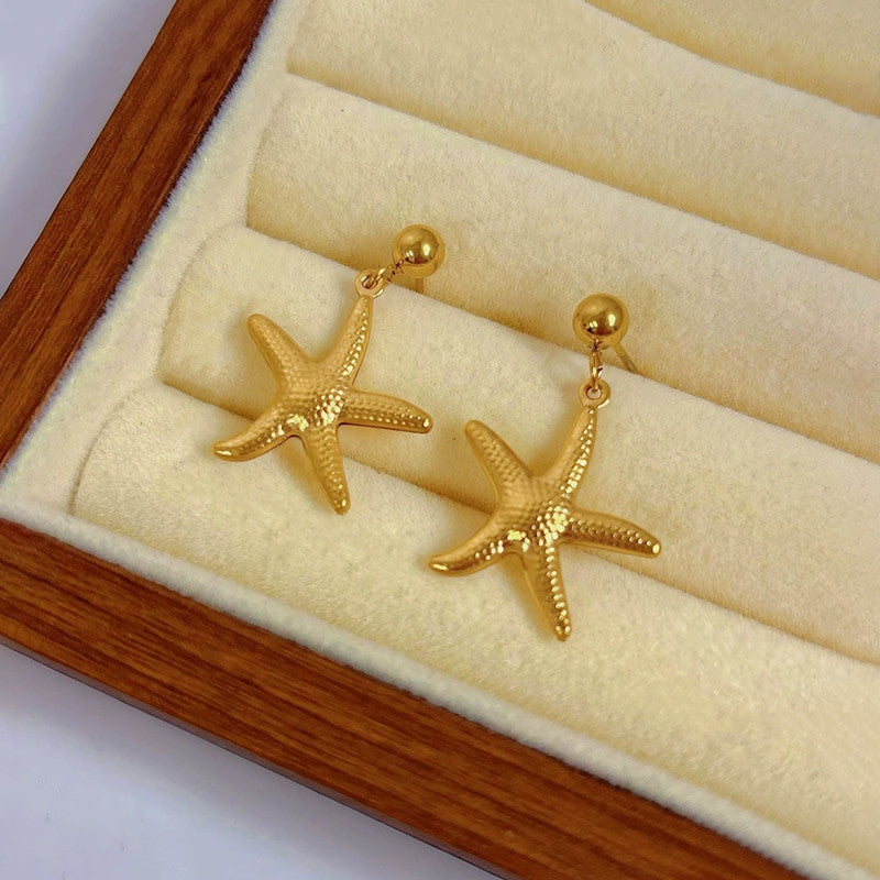 Gold starfish earrings on a wooden display box with beige interior