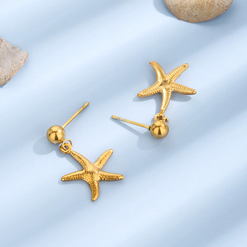 Gold starfish earrings on a light blue background with stones.