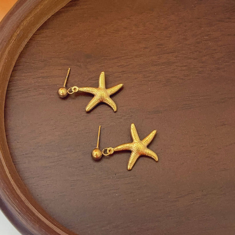 Gold starfish earrings on a wooden surface