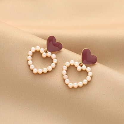 Heart-shaped earrings with pearl-like beads on a beige fabric background