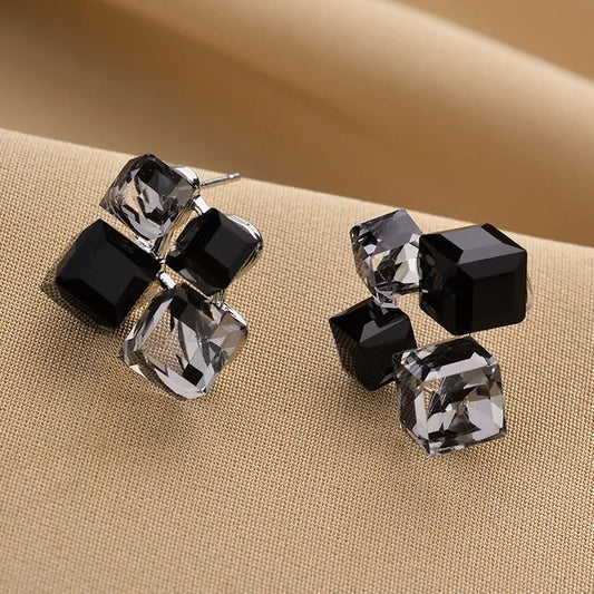 Pair of black and clear cube-shaped earrings on a beige fabric background