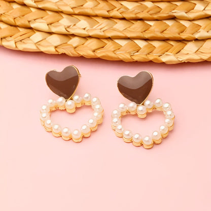 Heart-shaped earrings with pearl detailing on a pink background